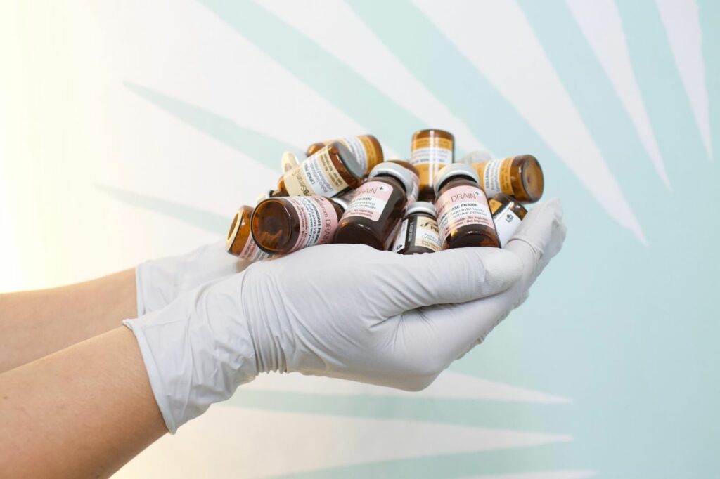 A close-up of gloved hands holding multiple medicine bottles against a light background.