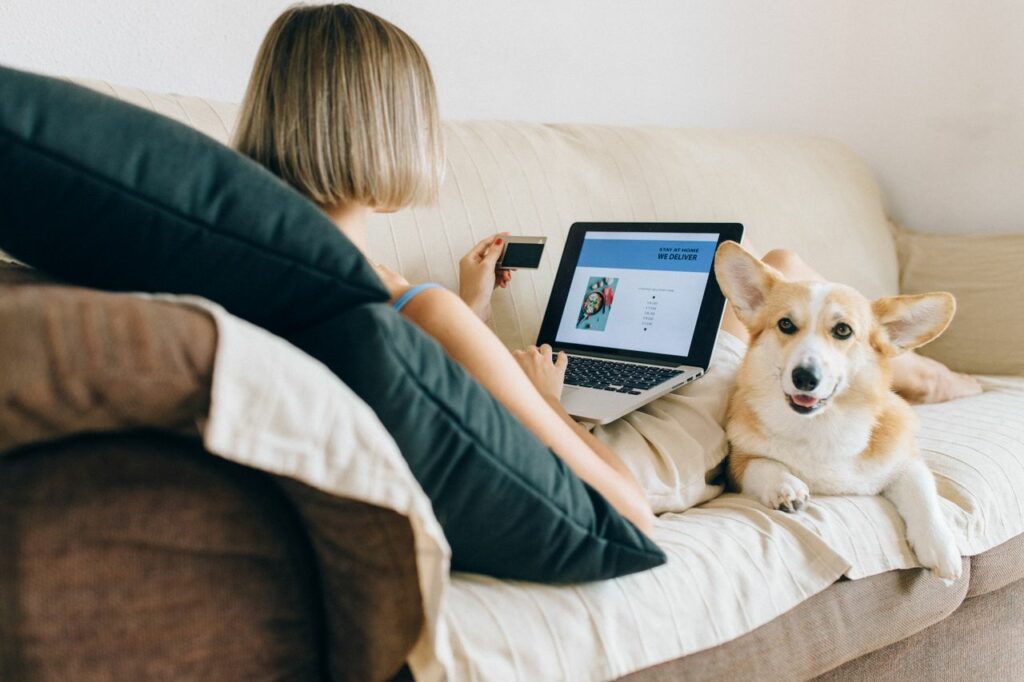 Femme qui utilise son ordinateur pour un suivi en ligne, avec son corgi couché à côté d'elle sur le canapé